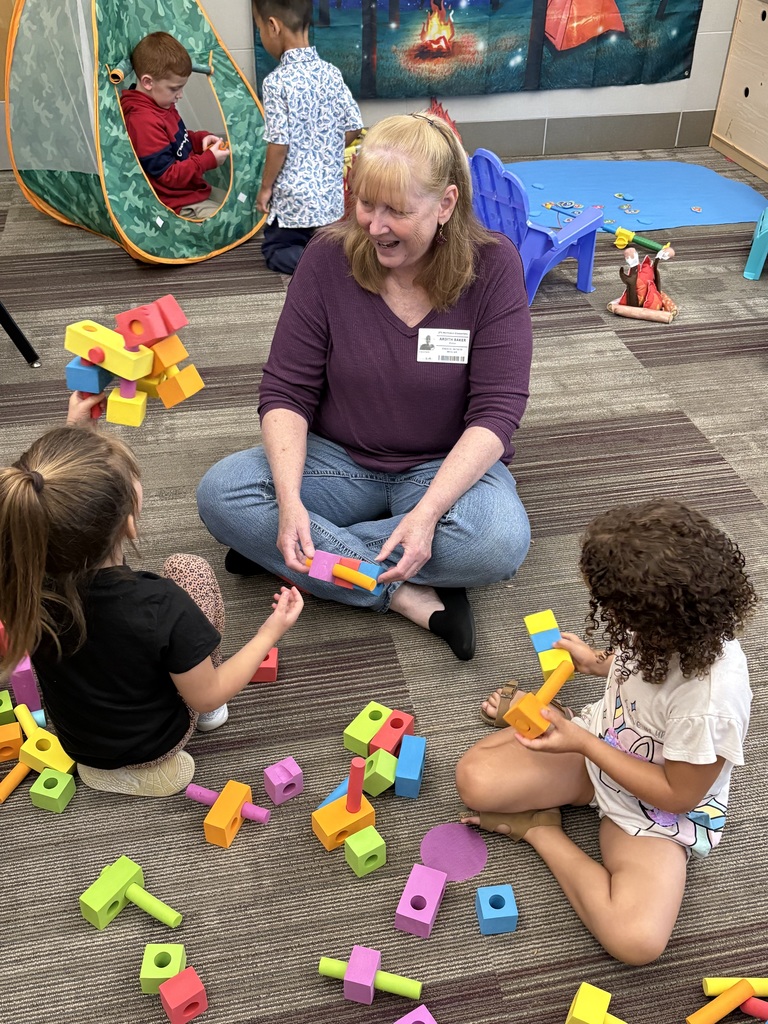  Senior living resident on the floor with two Pre-K students playing with blocks