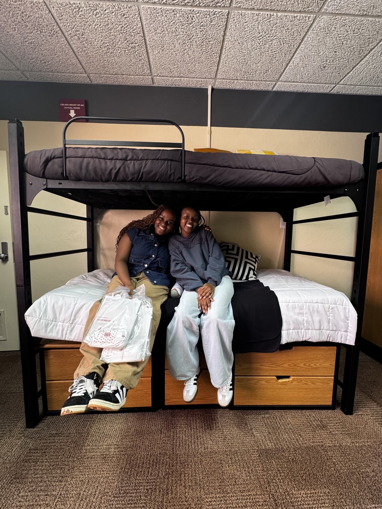 Two girls sitting on a bed in a dorm room at the University of Oklahoma