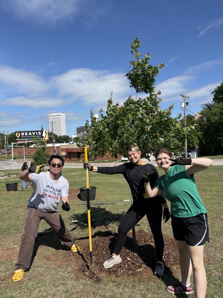 Three students posing by the tree they just planted