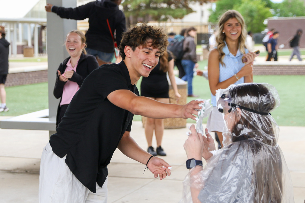 student pieing a teacher in the face. two girls behind laughing