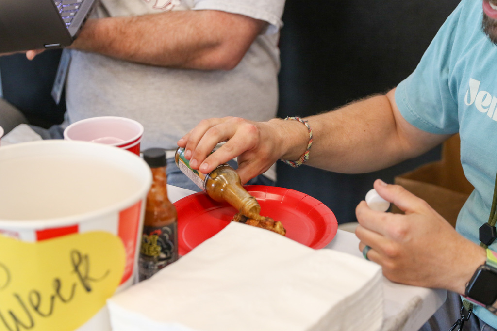 close up shot of a teach applying "the last dab" which is sauce directly to a wing