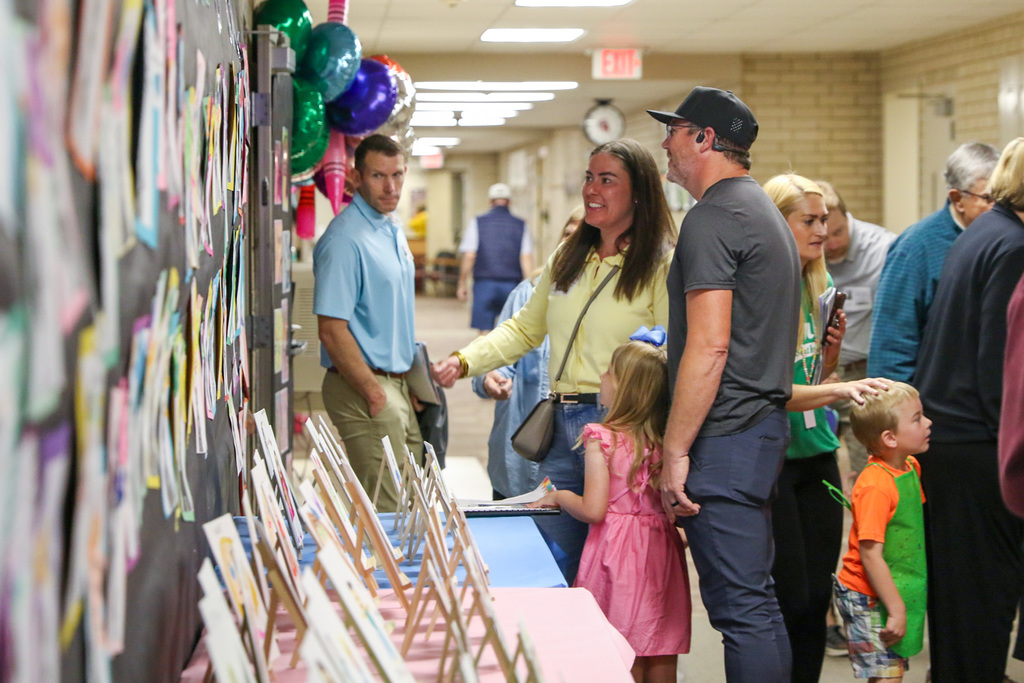 parents with their daughter looking at a wall of pre-k art work