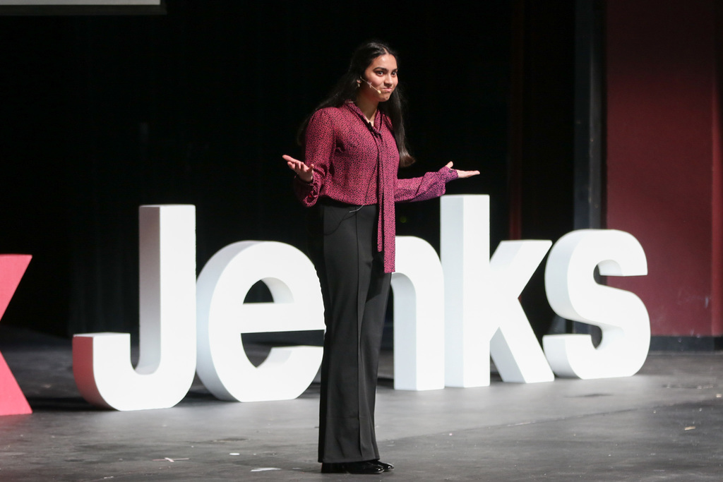 Student on stage with her arms out next to her. Jenks letters is behind her on the stage