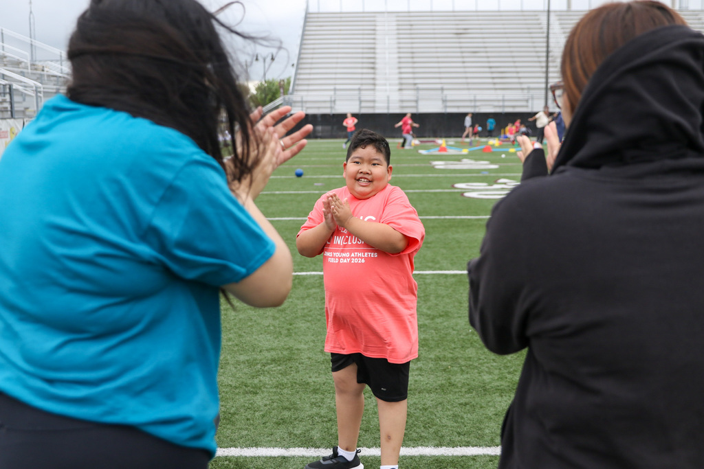 boy clapping in the center of the photo and on the sides you see the backs of two volunteers clapping with him