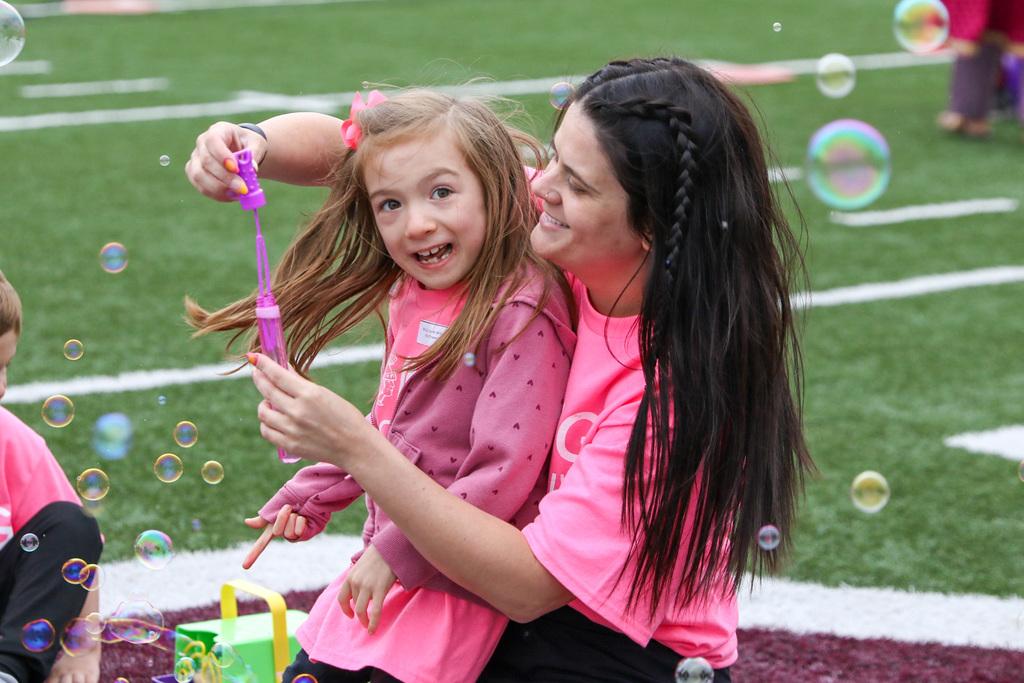 a staff member on her knees with a student athlete leaning against her. staff member is pulling the blow stick out of the bubbles. bubbles all around them