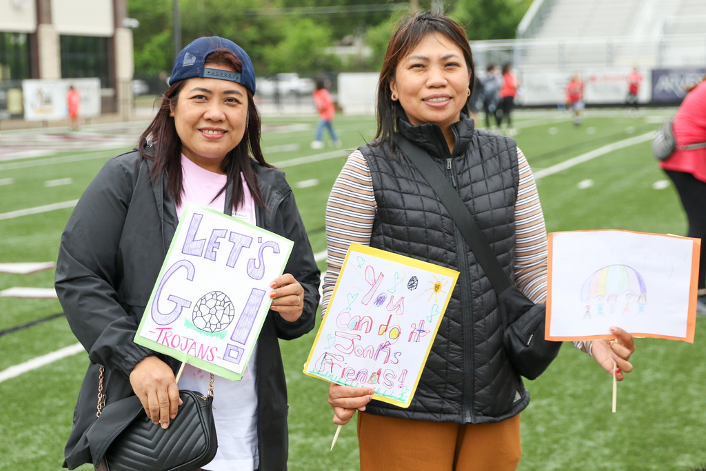 two parents with signs that say say lets go trojans