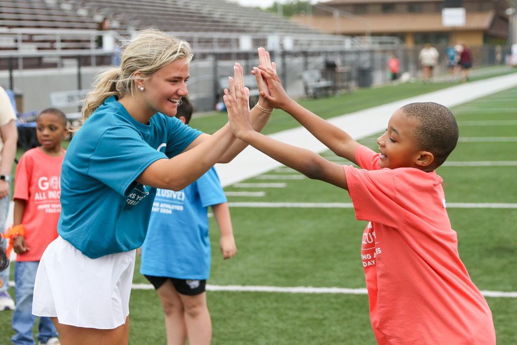 a high school student volunteer high fiving a young athlete