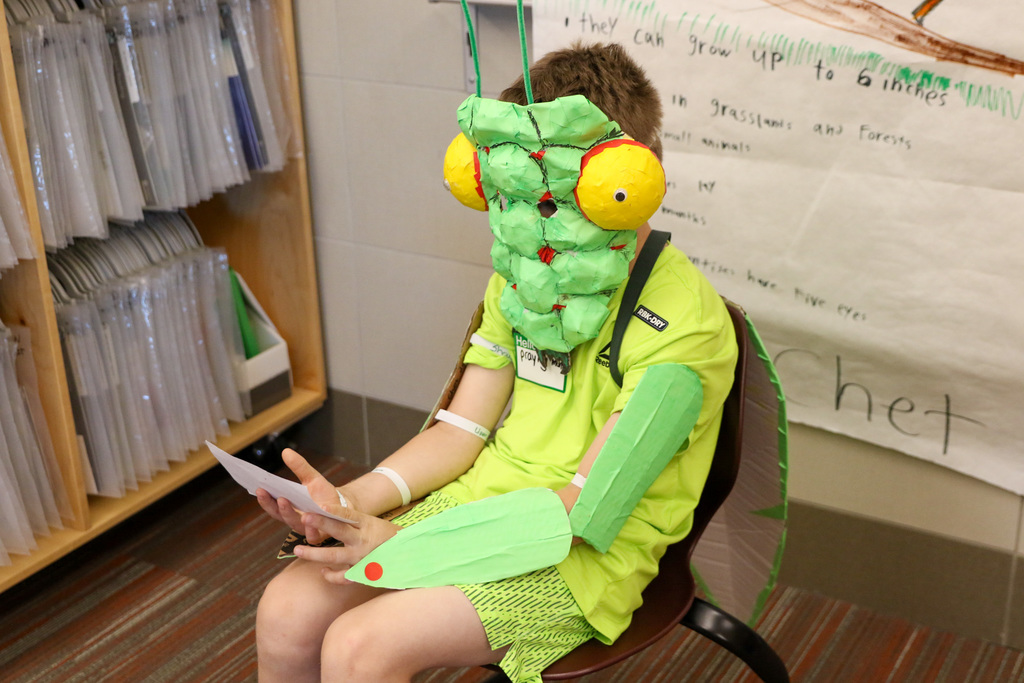 boy reading his presentation card in a praying mantis mask