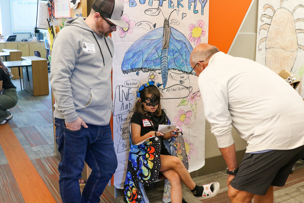 girl dressed up as a butterfly with two men next to her listening to her presentation