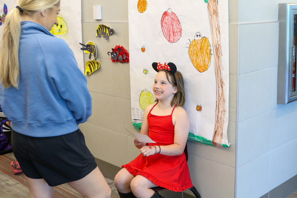girl dressed in red like a lady bug smiling up at a parent while presenting