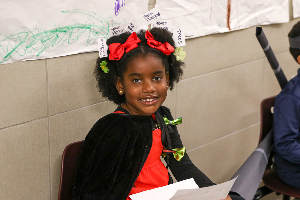 girl dressed as a lady bug. she has flower cards in her hair that say where she would be as a lady bug like trees or playground or flowers