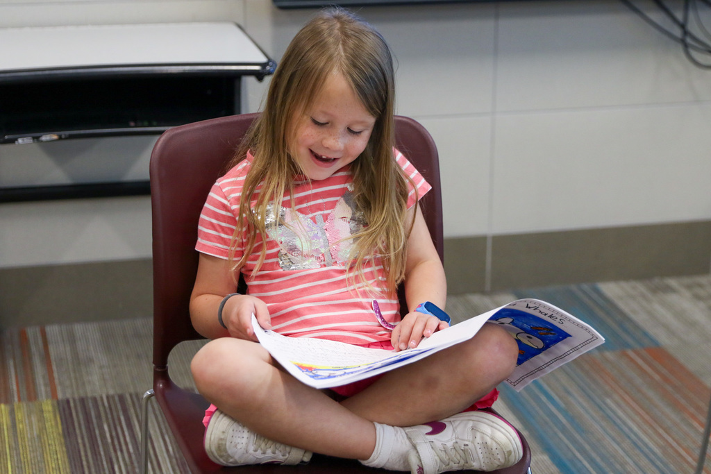 girl sitting in a chair with her book in her lap reading from it outloud