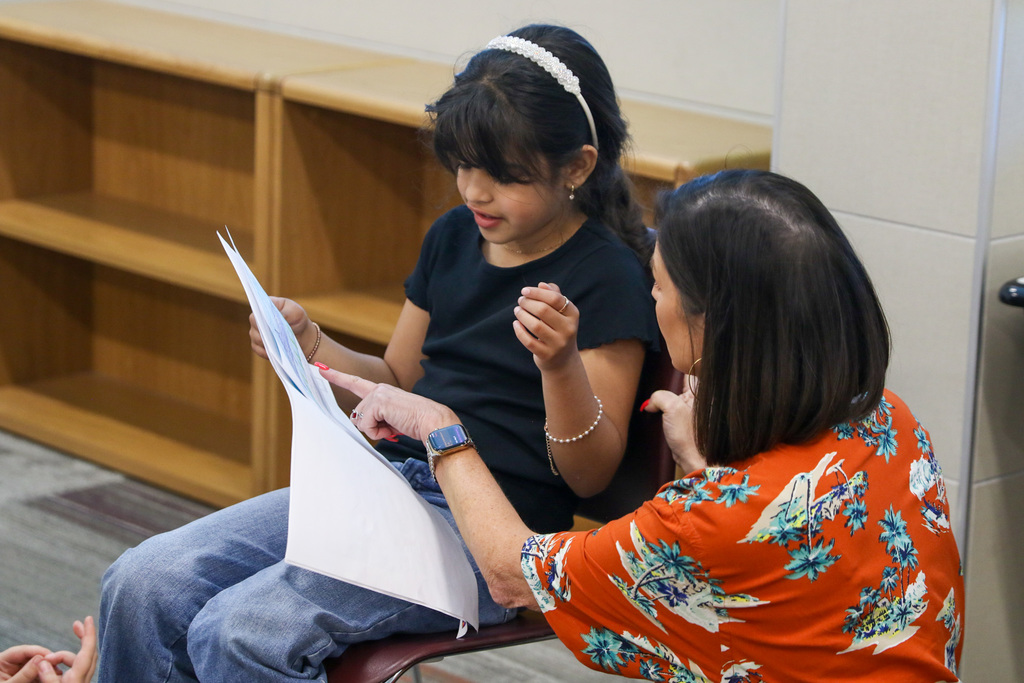 teacher helping a student with a word in her research book