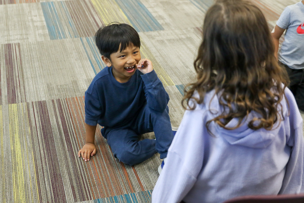 boy sitting on the ground looking at the presenting student smiling