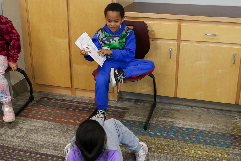 boy smiling to the girl on the ground pointing at the drawing on his book