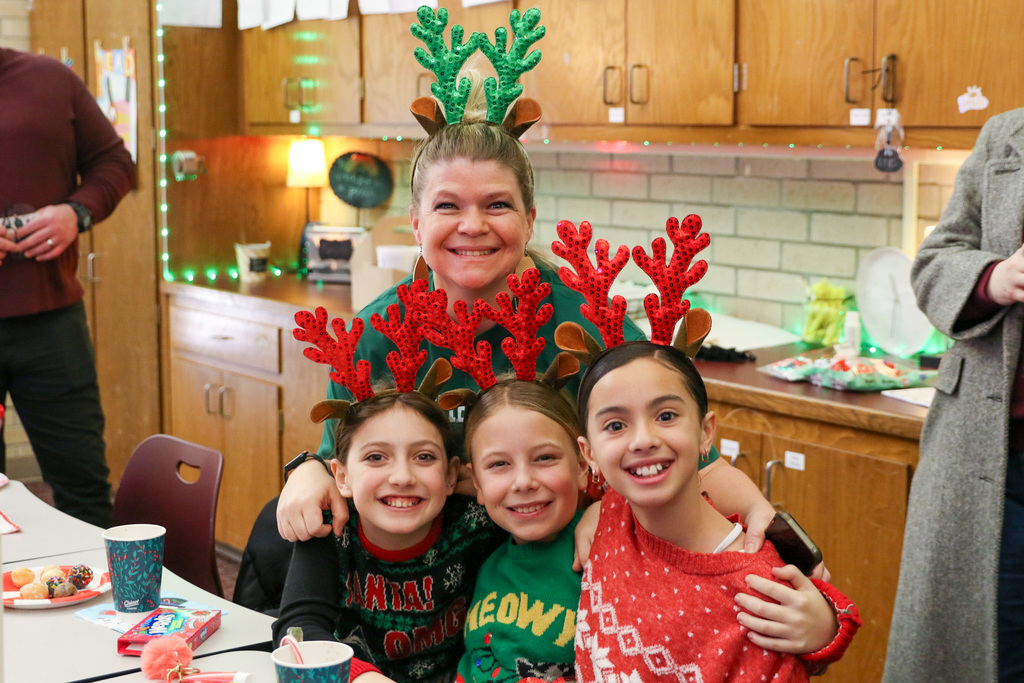teacher and three girls with matching christmas antler headbands smiling for a picture