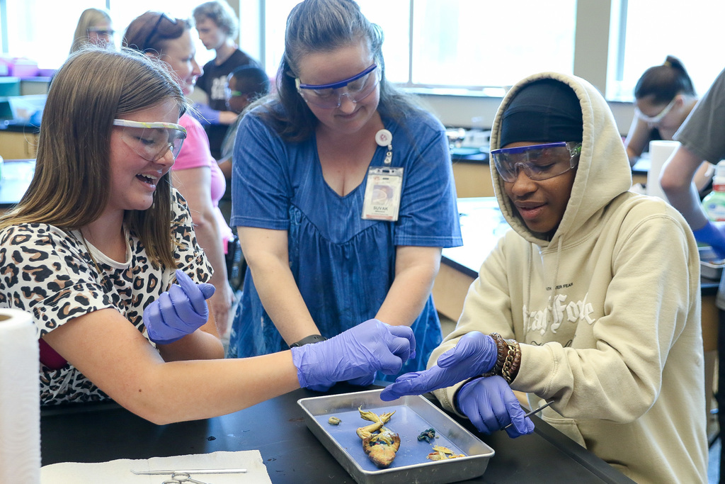 teacher in between two students who are dissecting frog