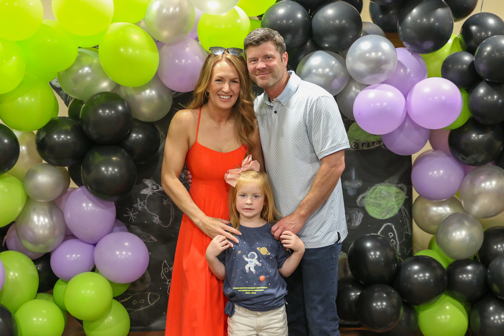 parents with their daughter smiling in front of a balloon backdrop