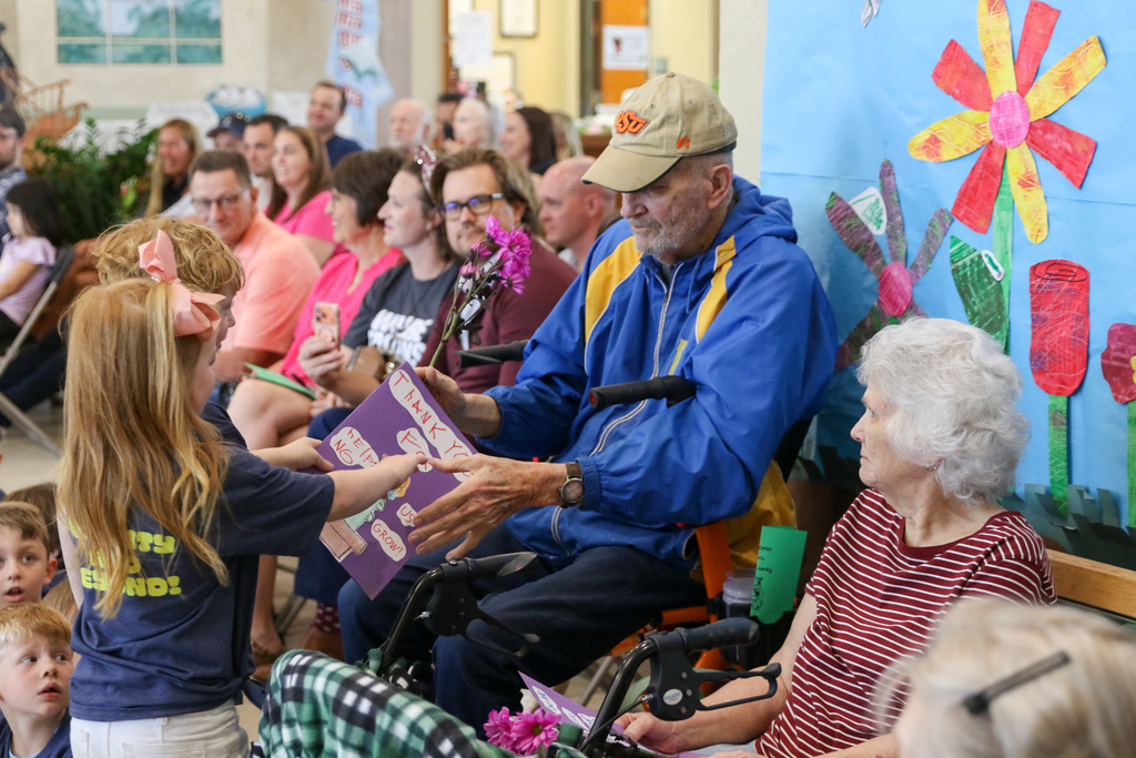 a boy and girl giving a flower and card  to a grandpa 