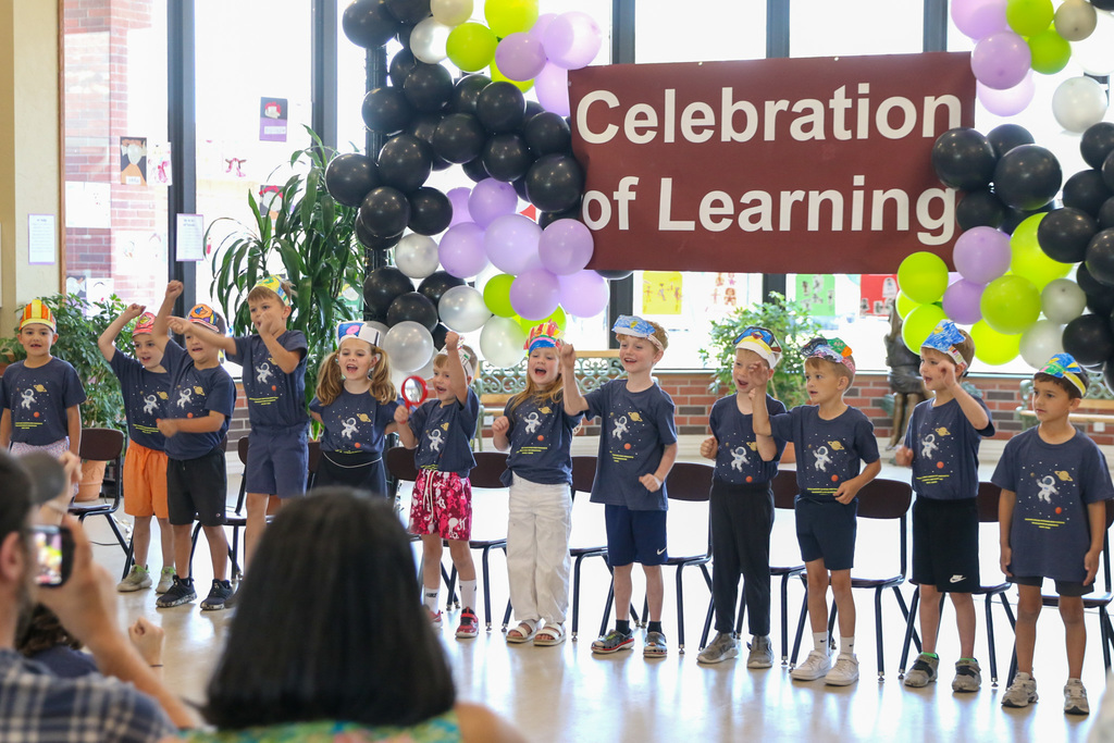 kindergarteners at Grace standing up infront of a balloon arrangement and a banner that says celebration of learning. students are singing a song