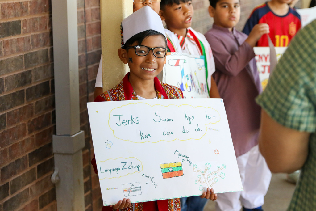boy holding up a sign that says enks siainn kya tekae ccia due oh