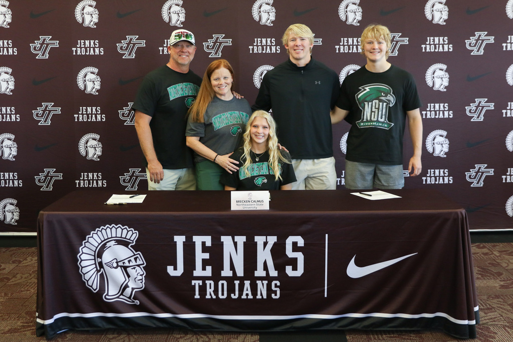Brecken with her family standing behind him as she sits at the signing table for a photo