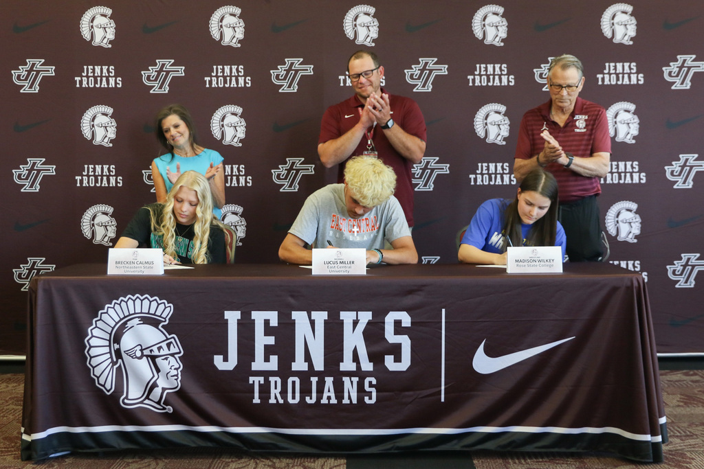 photo of all three students signing their letter of intent with their coach standing behind them