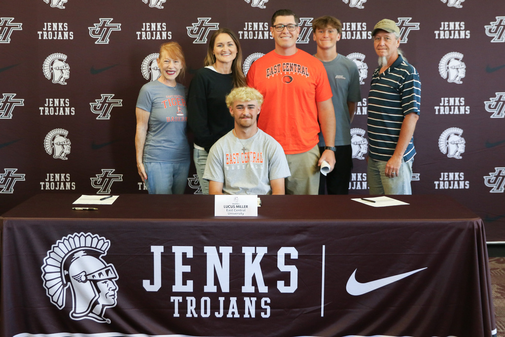 Lucus with his family standing behind him as he sits at the signing table for a photo