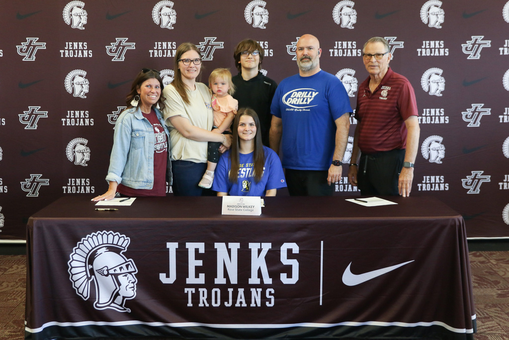 Madison with her family standing behind him as she sits at the signing table for a photo