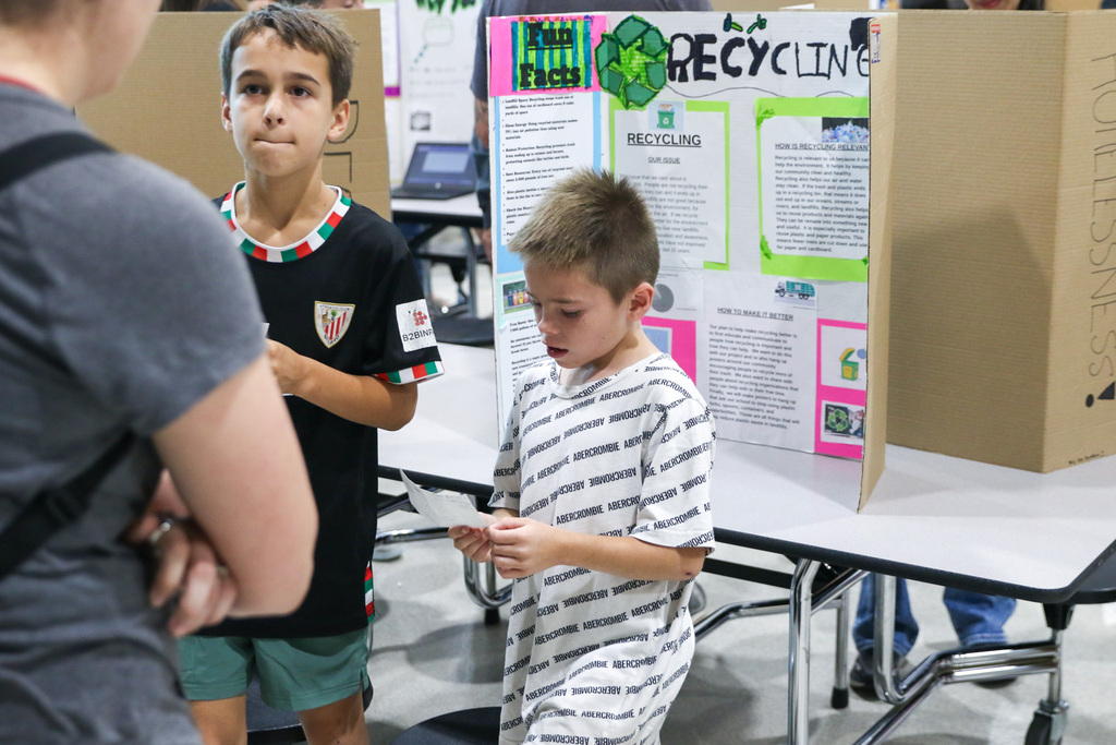 A fourth grade student presents to an adult visitor while standing beside an exhibition project display.