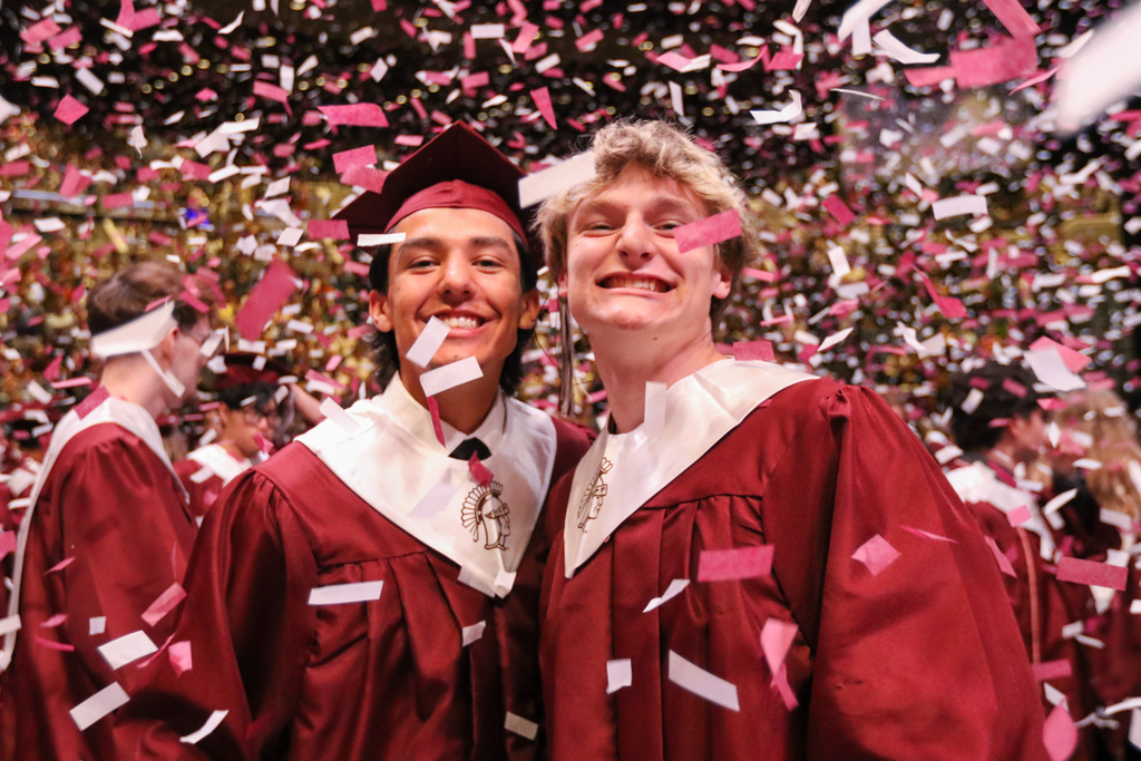 two boys in their caps and gowns with confetti falling all arouind them smiling for a photo