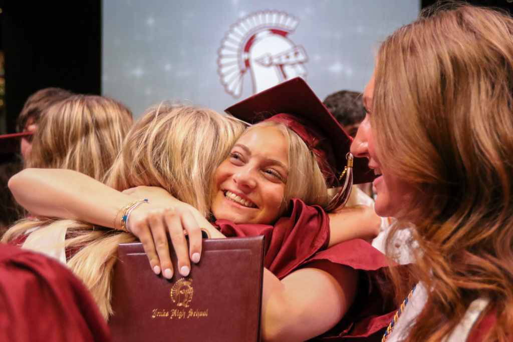 girl hugging a friend smiling big with her diploma in hand