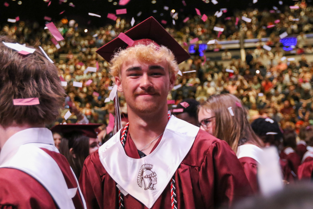 boy smiling with his cap and gown on for a photo with confetti falling around him