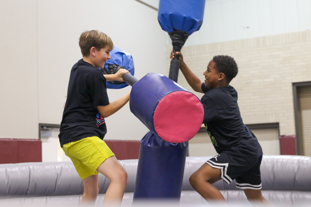 two boys using double ended foam sticks to knock each other off of a platform
