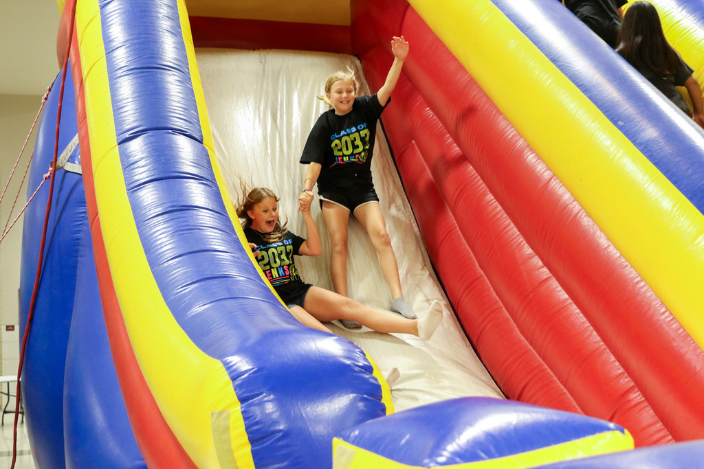 two girls sliding down the an inflatable slide. they are holding hands