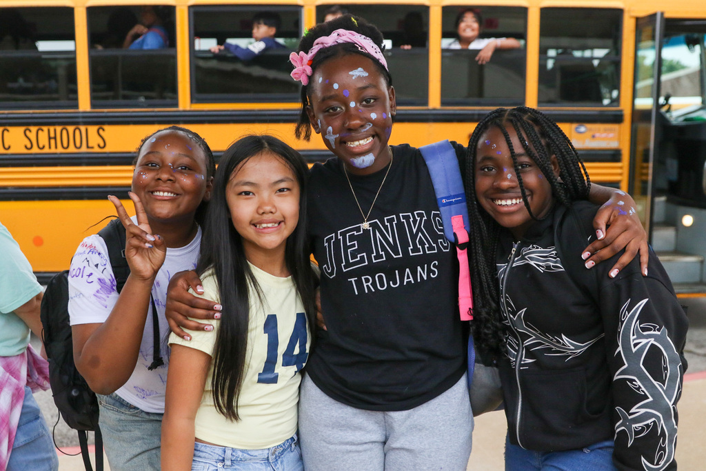 4 girls stand and pose for a photo infront of a bus