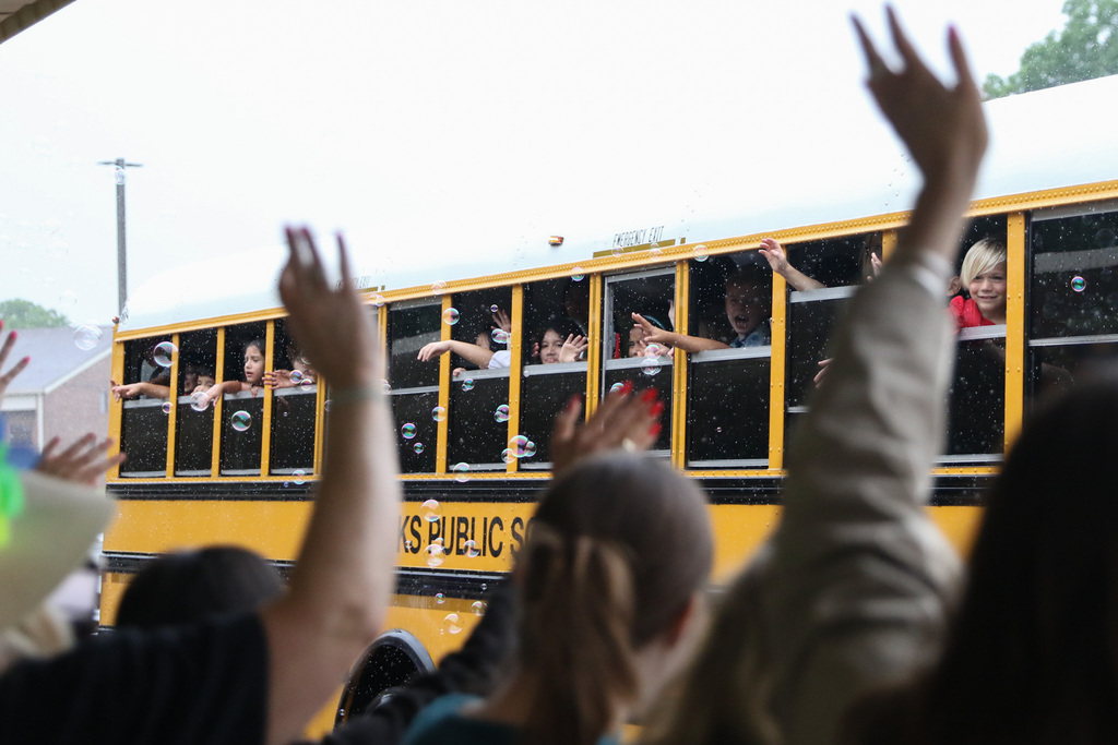 view from behind teachers as they wave to a bus of students who are waving back