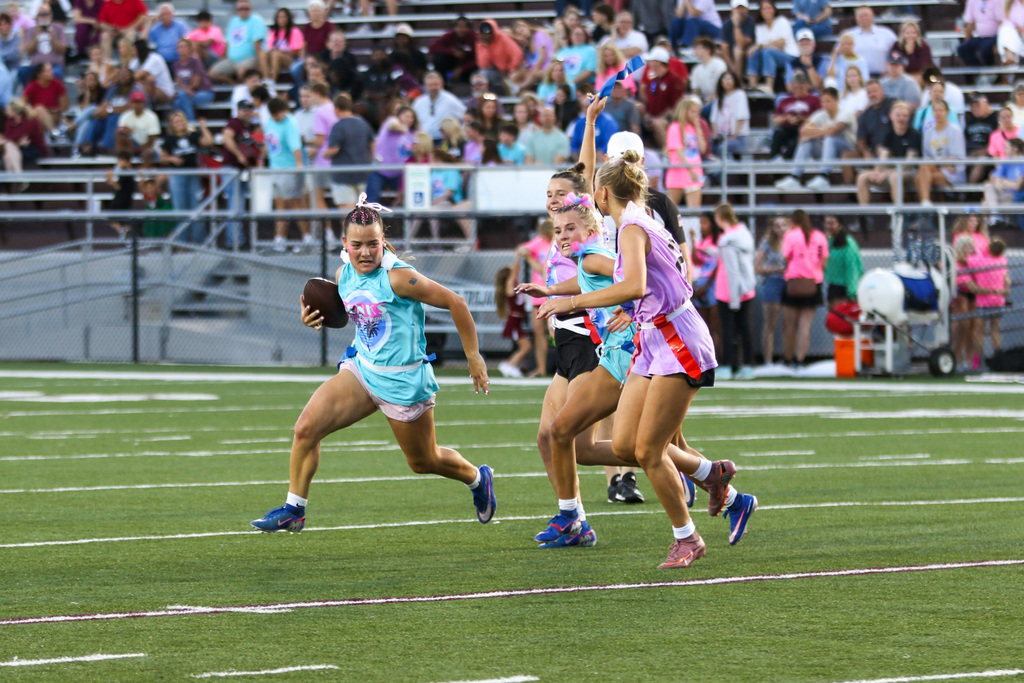 senior girl running the ball with a junior waving her flag in the air