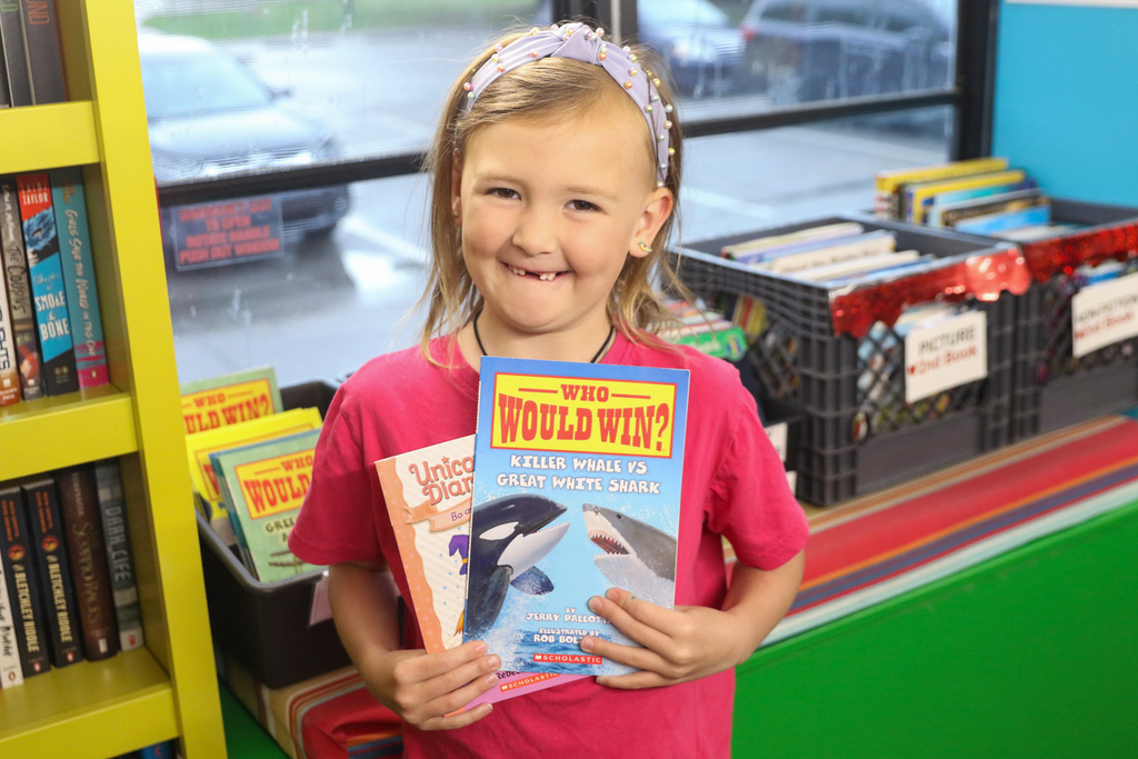 little girl holding her two books she chose smiling for a photo