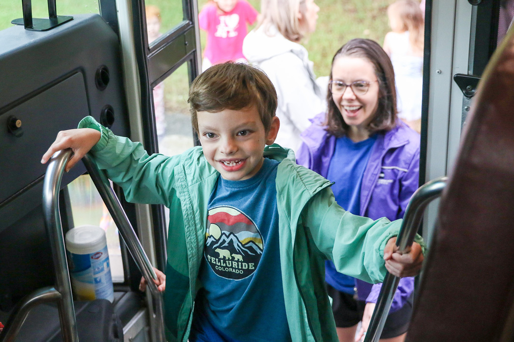 boy coming up the stairs to get on the bookmobile smiling at the driver