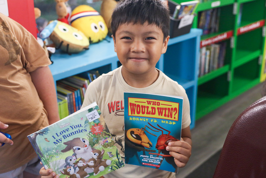 boy holding up two books he chose smiling for a photo