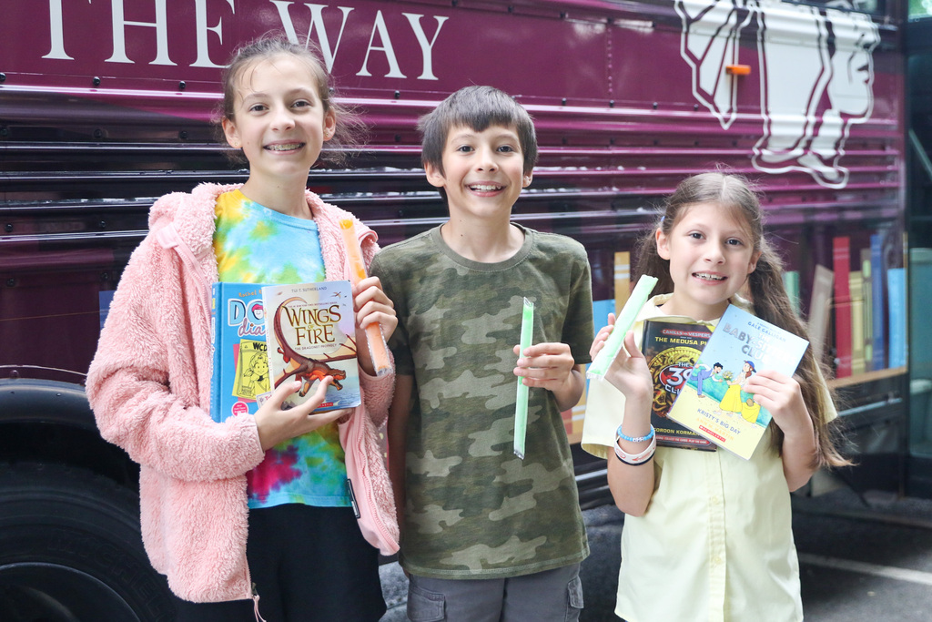 two girls and a boy in the middle of them holding their popsicles and books they chose outside of the bookmobile for a photo