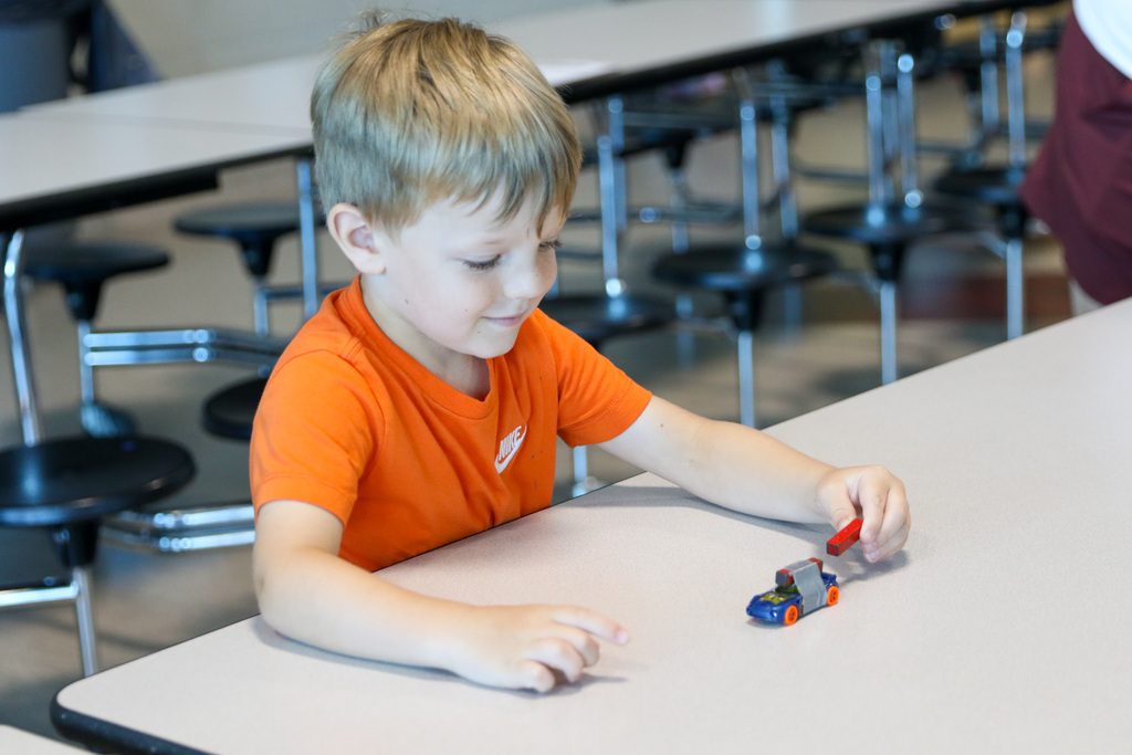 boy using the opposite end of a magnet to push a small car that has a magnet tapped to it