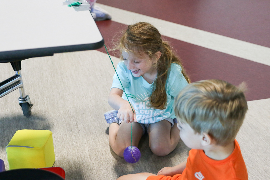 girl smiling using a ball tied to a rope to knock down foam blocks using force