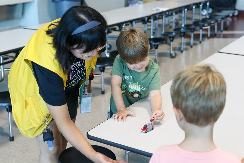 boy pushing car with a magnet while the discovery lab staff member is next to him with her hand at the edge of the table ready to catch it.