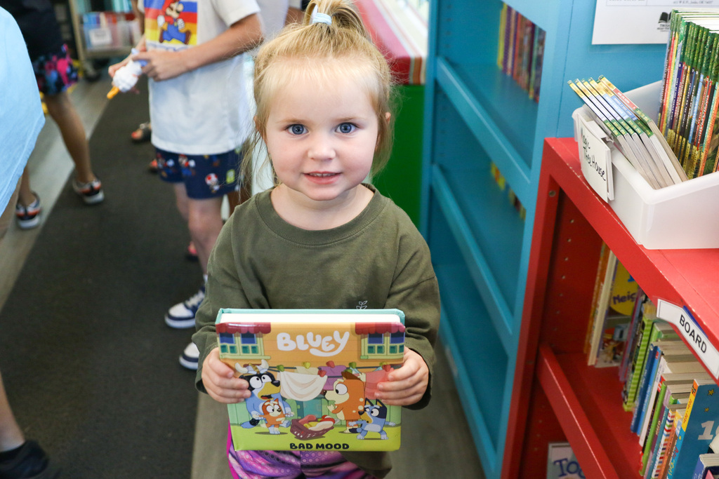 girl holding up a bluey book in the bookmobile smiling for a photo