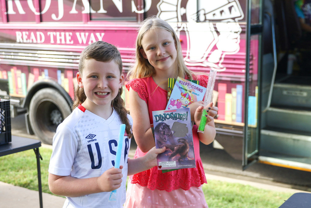 a boy and a girl holding up their books and popsicles outside the bookmobile smiling for a photo