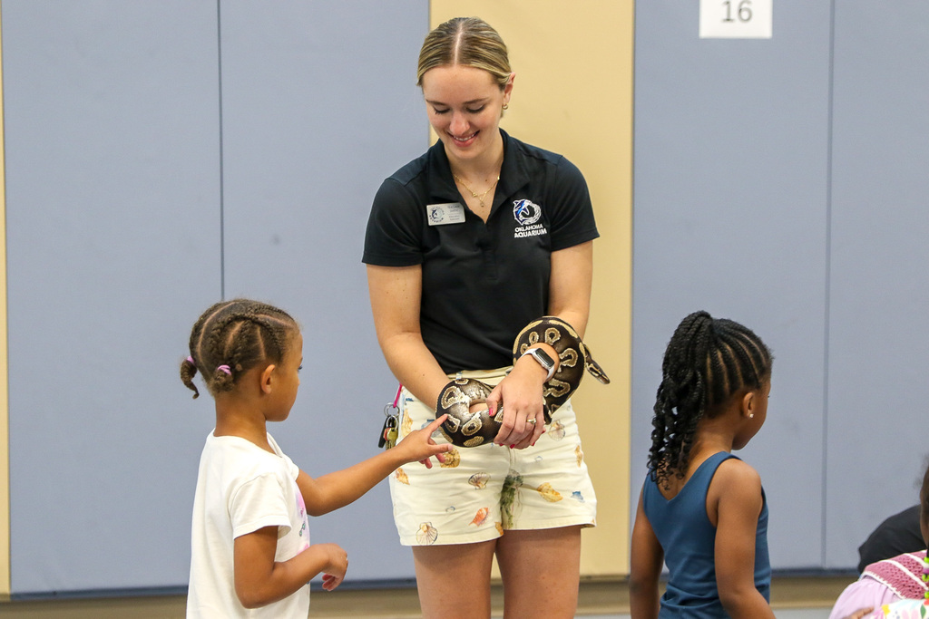 girl petting snake wrapped around instructors arm