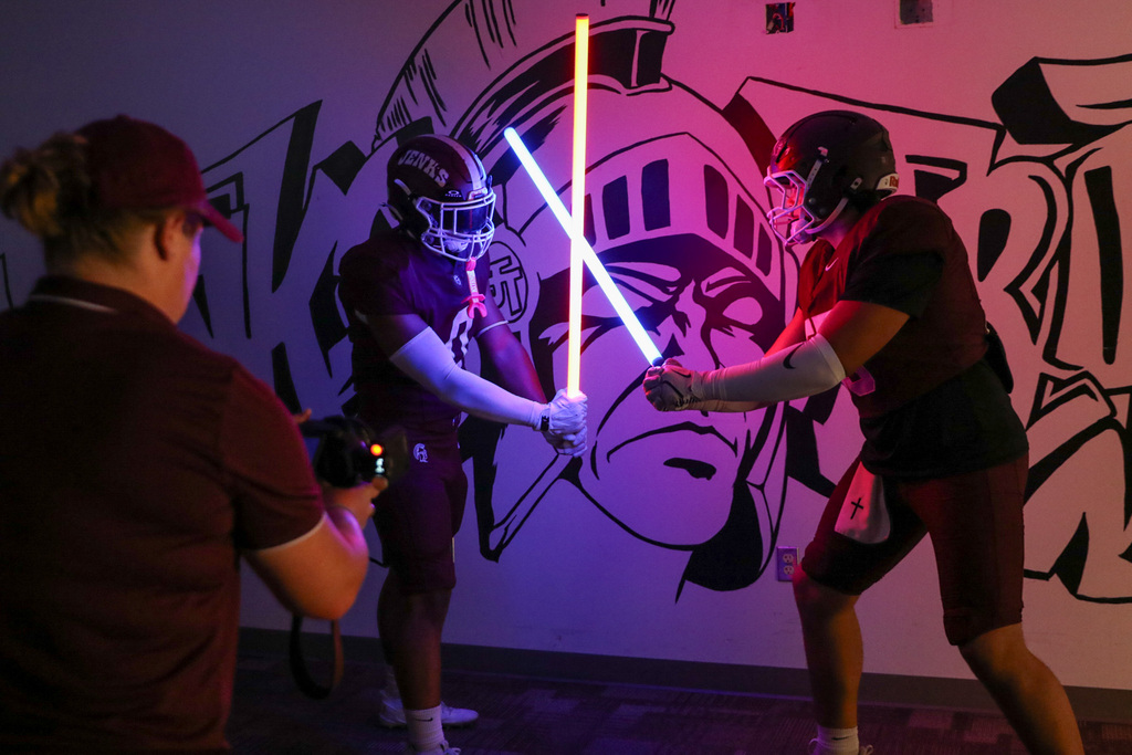 two boys with lights that look like light sabers standing against a mural that looks like graffiti that says jenks trojans with a trojan head in the middle of it.