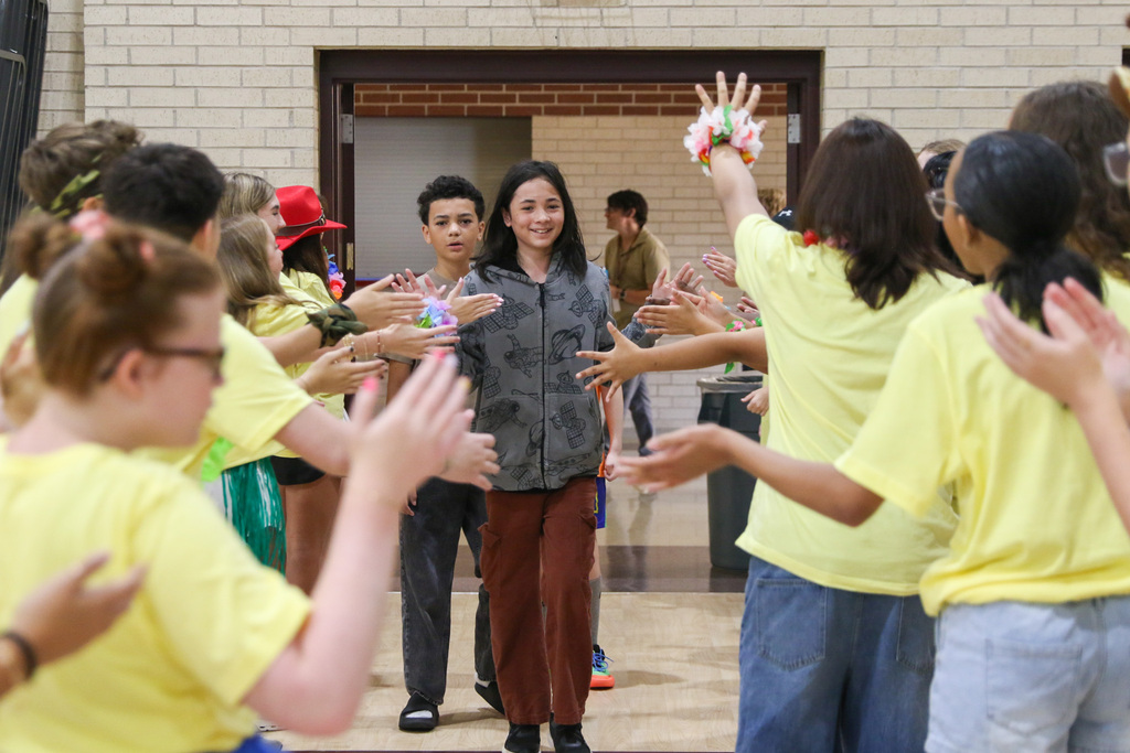 7th grade boy walking into orientation being greeted by 8th grade WEB leaders cheering for him and giving him high fives